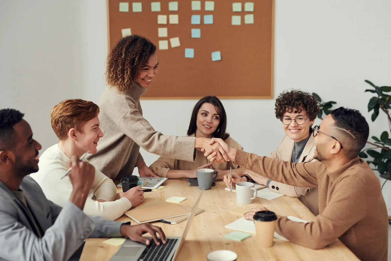 Colleagues shaking hands across a shared working table.